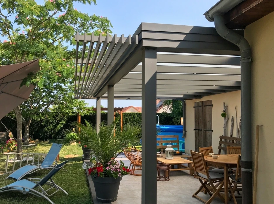 Terrasse extérieure couverte par une pergola bioclimatique à lames orientables en aluminium anthracite, fixée en appui mural