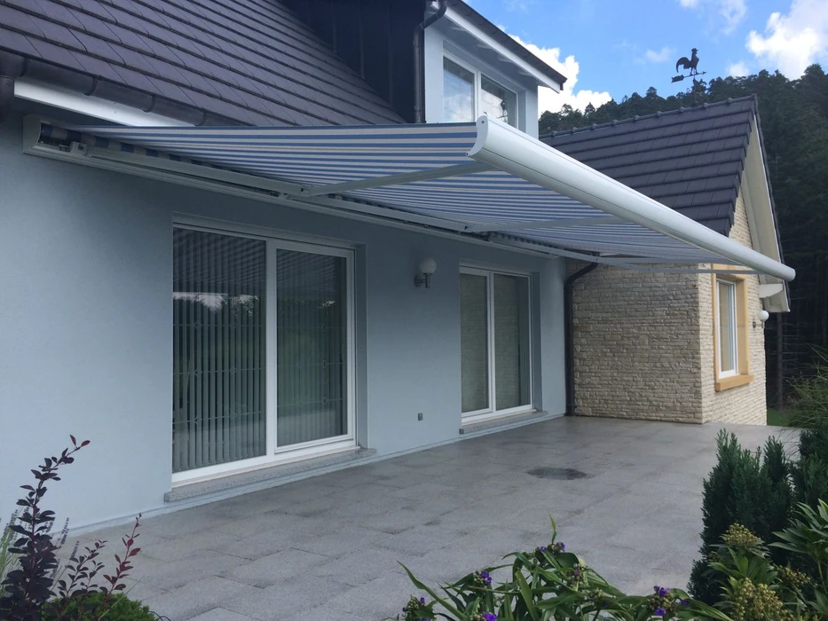 Volet coulissant en aluminium gris clair installé en façade extérieure d'une maison, partiellement ouvert devant une baie vitrée à deux vantaux avec rideau blanc