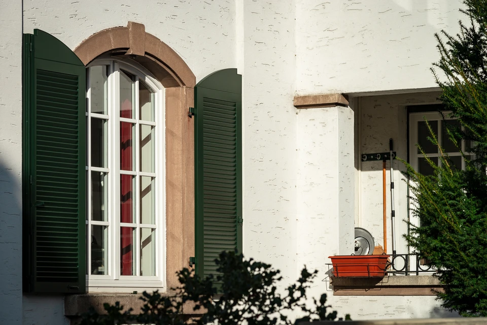 Façade en pierre calcaire avec une baie vitrée coulissante PVC blanc double vitrage, encadrée de volets battants bois peints vert amande (RAL 6021)