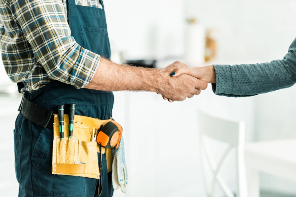 Homme en tenue de travail installant une baie vitrée coulissante à cadre anthracite dans maison en construction